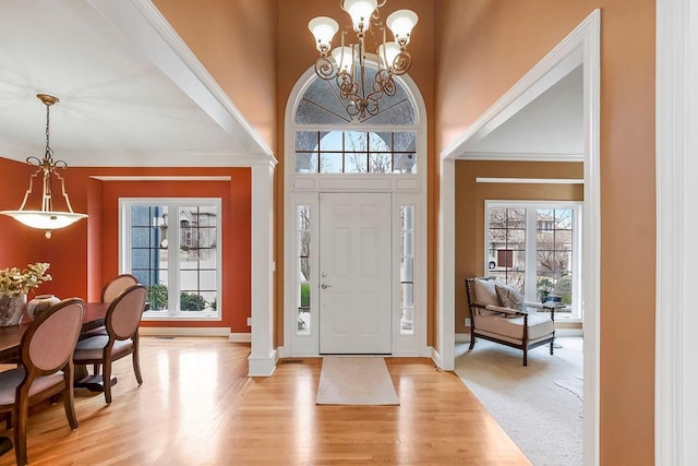 entryway with an inviting chandelier, a healthy amount of sunlight, light wood-type flooring, and a high ceiling