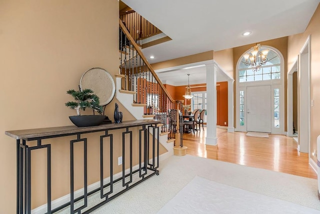 entrance foyer with light wood-type flooring, a towering ceiling, decorative columns, and a notable chandelier