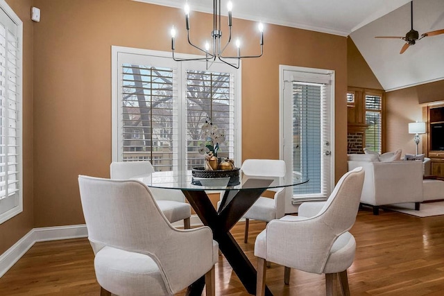 dining room featuring ceiling fan with notable chandelier, wood-type flooring, and vaulted ceiling