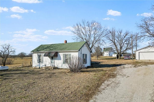 view of front facade featuring a detached garage, a chimney, and an outbuilding