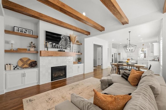 living room featuring dark hardwood / wood-style floors, beam ceiling, a tile fireplace, and a notable chandelier