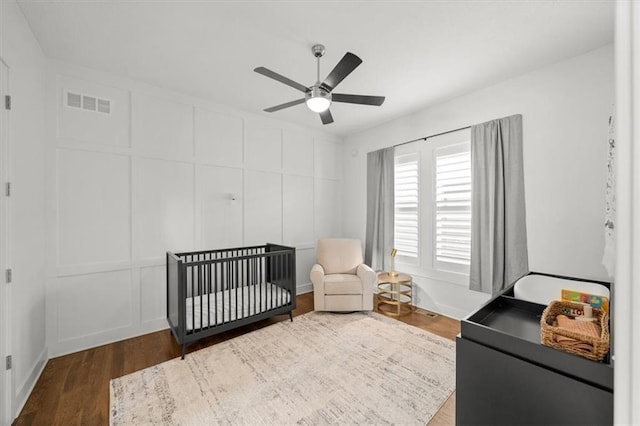 bedroom with a nursery area, ceiling fan, and dark hardwood / wood-style floors