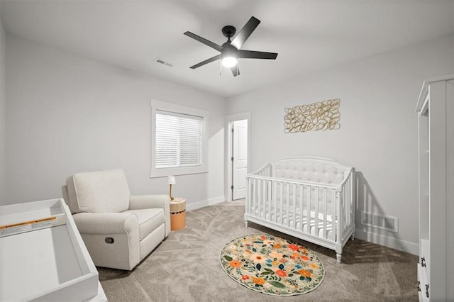 carpeted bedroom featuring ceiling fan and a crib