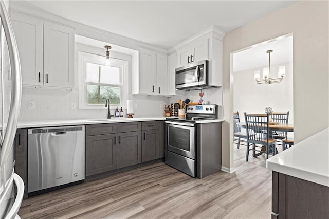 kitchen featuring sink, decorative light fixtures, stainless steel appliances, light hardwood / wood-style floors, and white cabinets