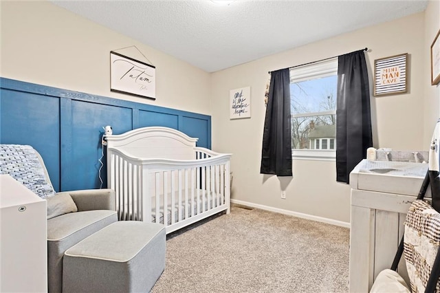 bedroom featuring a nursery area, light colored carpet, and a textured ceiling