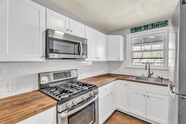 kitchen featuring white cabinetry, butcher block countertops, appliances with stainless steel finishes, and a sink