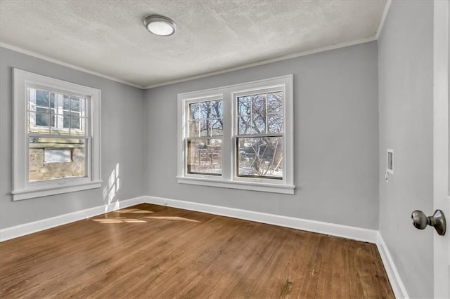 empty room featuring a textured ceiling, ornamental molding, wood finished floors, and baseboards