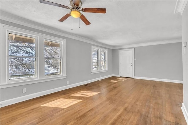 interior space with baseboards, ornamental molding, ceiling fan, and wood finished floors