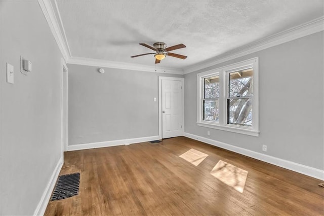 empty room with ornamental molding, visible vents, baseboards, and wood finished floors