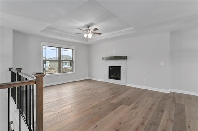 unfurnished living room with a raised ceiling, ceiling fan, and light wood-type flooring