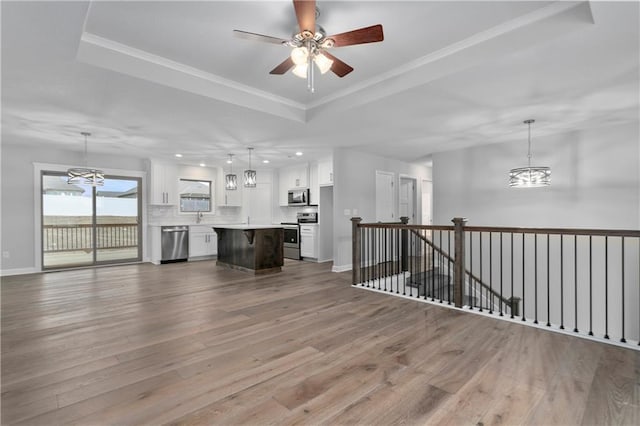 unfurnished living room with a raised ceiling, wood-type flooring, ornamental molding, and ceiling fan with notable chandelier