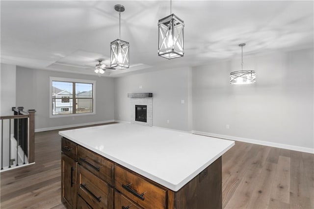 kitchen with a stone fireplace, hanging light fixtures, a raised ceiling, hardwood / wood-style flooring, and ceiling fan