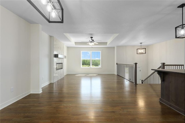 1320 N Holland Ct, Independence, MO 64056 - unfurnished living room featuring dark wood-style flooring, a tray ceiling, ceiling fan, and a chandelier