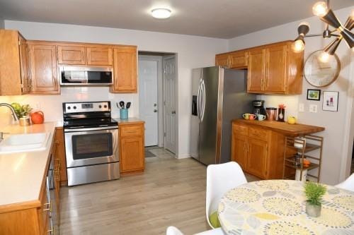 kitchen with stainless steel appliances, light hardwood / wood-style floors, sink, and hanging light fixtures