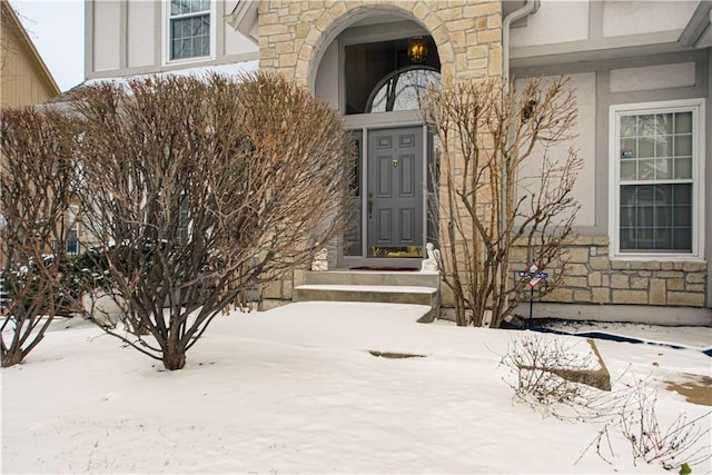 snow covered property entrance with stone siding and stucco siding