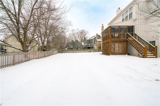 yard covered in snow with a residential view, a sunroom, a fenced backyard, and stairway