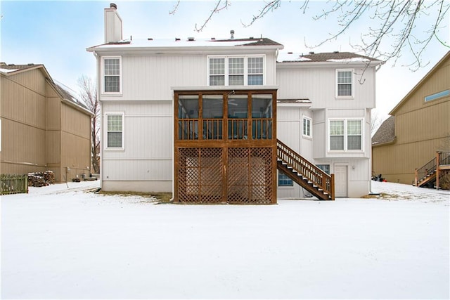 snow covered rear of property with stairway, a chimney, and a sunroom