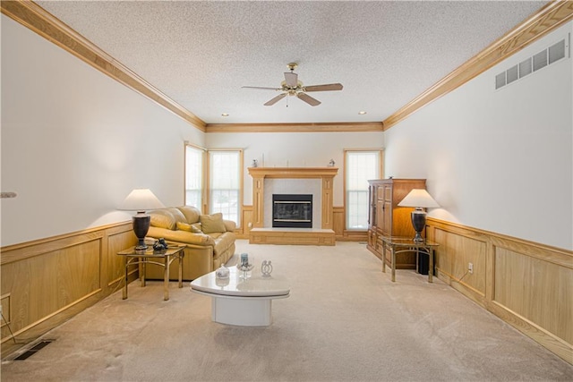 carpeted living area with a textured ceiling, wainscoting, a glass covered fireplace, and visible vents