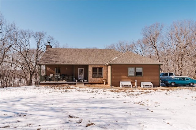 snow covered property with a porch and a chimney