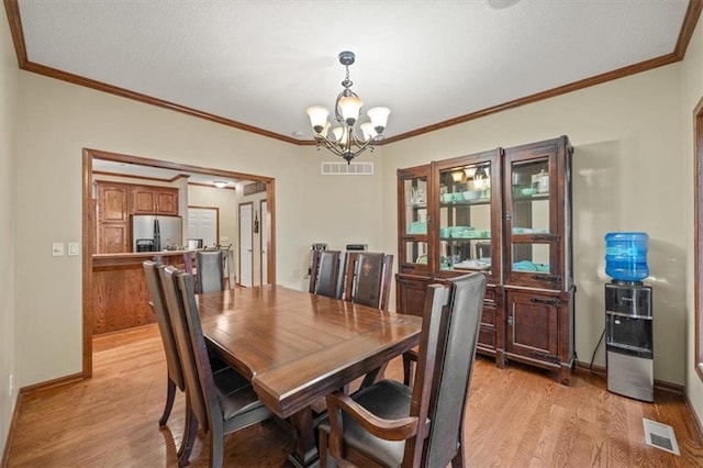 dining space with crown molding, an inviting chandelier, and light hardwood / wood-style flooring