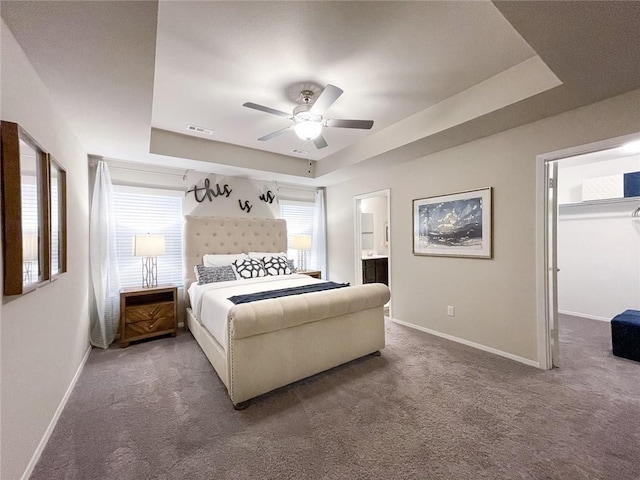 bedroom featuring connected bathroom, a walk in closet, carpet flooring, a tray ceiling, and ceiling fan