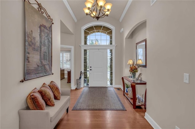 entrance foyer with a notable chandelier, wood finished floors, baseboards, vaulted ceiling, and crown molding