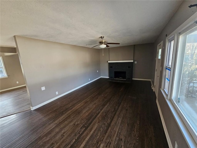 unfurnished living room featuring dark hardwood / wood-style flooring, a brick fireplace, a healthy amount of sunlight, and ceiling fan