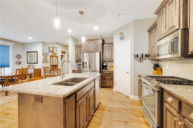 kitchen with sink, a kitchen island with sink, light stone counters, light hardwood / wood-style floors, and stainless steel appliances