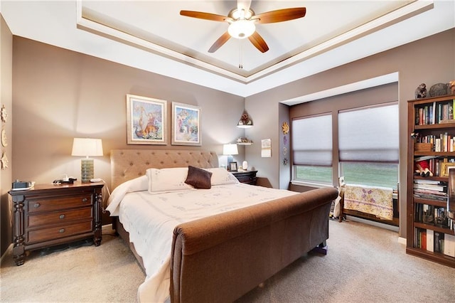 carpeted bedroom with ceiling fan and a raised ceiling