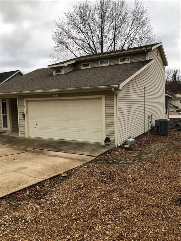 view of side of property featuring a garage, roof with shingles, driveway, and central air condition unit