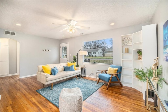 living room with a textured ceiling, wood-type flooring, and ceiling fan