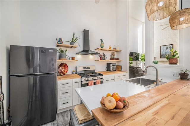 kitchen featuring butcher block countertops, wall chimney range hood, sink, appliances with stainless steel finishes, and white cabinetry