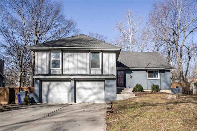 split level home featuring fence, roof with shingles, concrete driveway, a garage, and brick siding