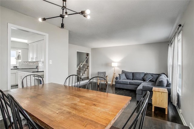 dining space featuring baseboards, stairs, a notable chandelier, a textured ceiling, and dark wood-style flooring