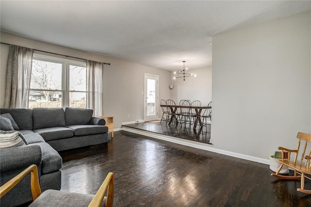 living room featuring an inviting chandelier, a textured ceiling, baseboards, and wood finished floors