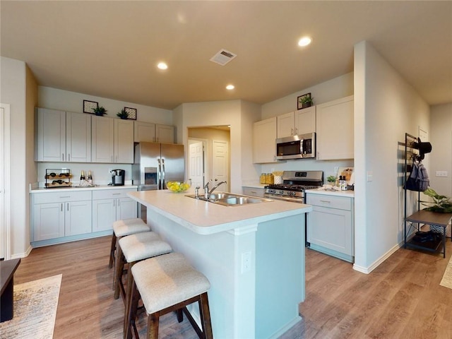 kitchen featuring sink, appliances with stainless steel finishes, white cabinetry, an island with sink, and a kitchen bar