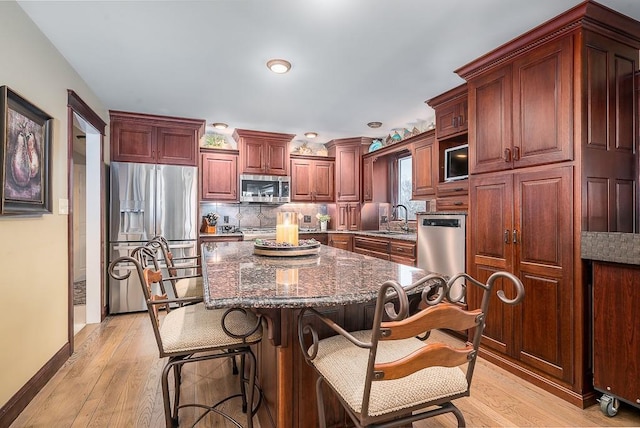 kitchen featuring light wood finished floors, a center island, decorative backsplash, stainless steel appliances, and a sink