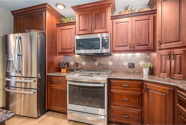 kitchen featuring dark stone counters, tasteful backsplash, appliances with stainless steel finishes, and light wood-style flooring