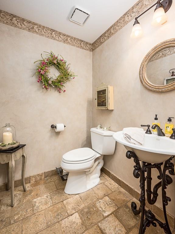 bathroom with stone tile floors, visible vents, toilet, and baseboards