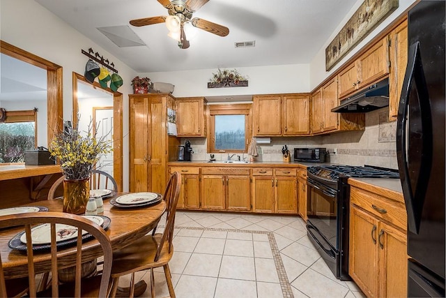 kitchen featuring visible vents, under cabinet range hood, light tile patterned floors, brown cabinetry, and black appliances