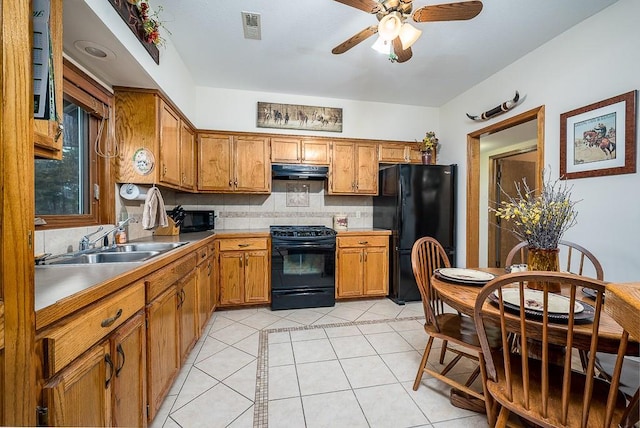 kitchen with under cabinet range hood, light tile patterned floors, brown cabinetry, black appliances, and a sink