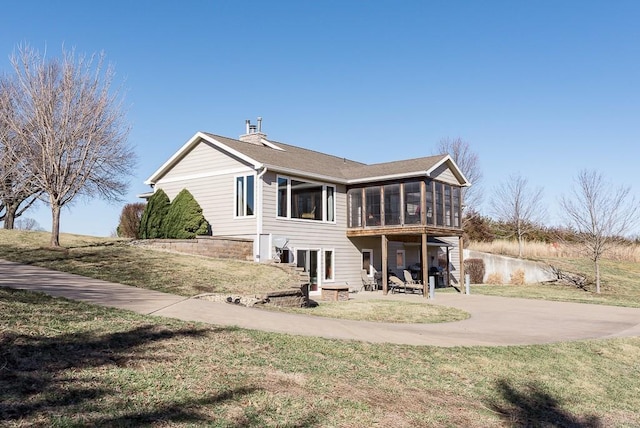 rear view of property with a patio, driveway, a yard, a sunroom, and a chimney