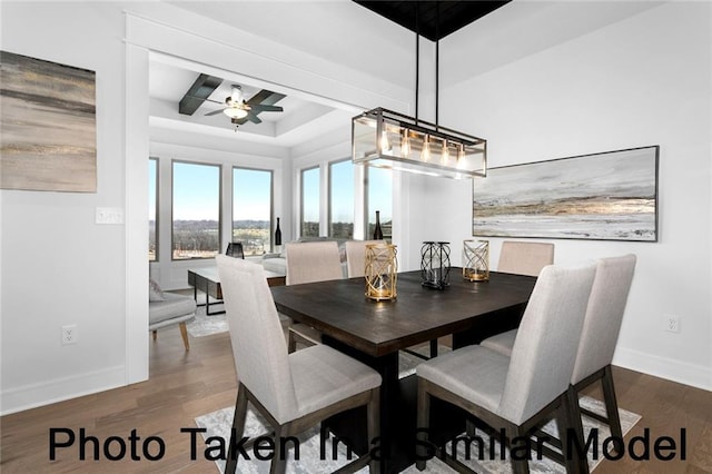 dining room featuring a ceiling fan, baseboards, a raised ceiling, and dark wood-style flooring