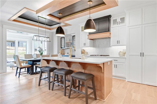 22109 W 93rd Ter, Lenexa, KS 66220 - kitchen featuring a tray ceiling, light wood-style flooring, a kitchen island with sink, light countertops, and decorative backsplash