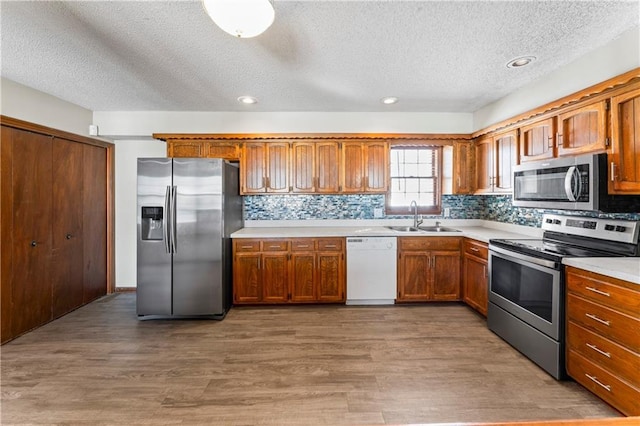 kitchen with appliances with stainless steel finishes, sink, a textured ceiling, hardwood / wood-style flooring, and decorative backsplash