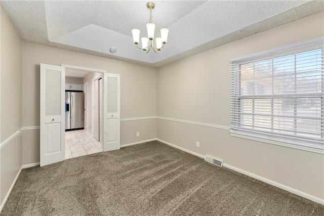 carpeted spare room with visible vents, baseboards, a textured ceiling, and an inviting chandelier