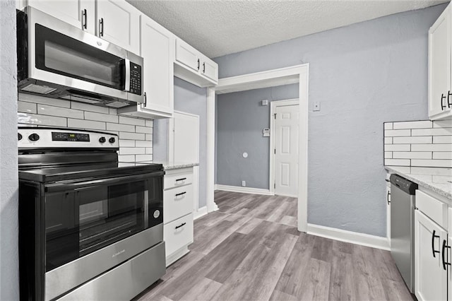 kitchen featuring white cabinetry, light stone counters, light hardwood / wood-style flooring, stainless steel appliances, and decorative backsplash