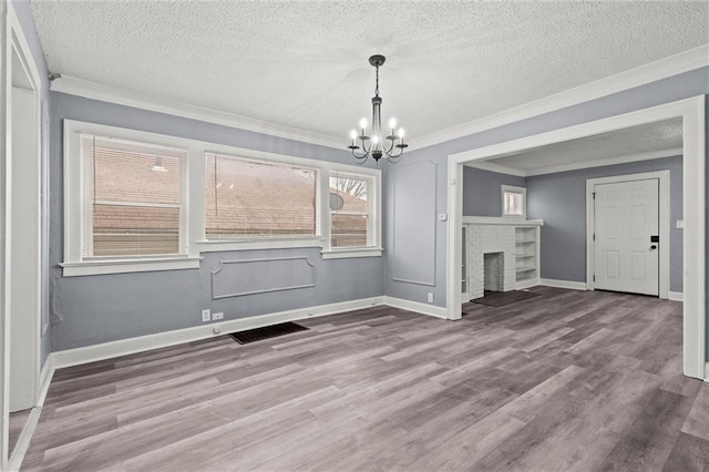 unfurnished dining area with an inviting chandelier, a fireplace, crown molding, and wood-type flooring