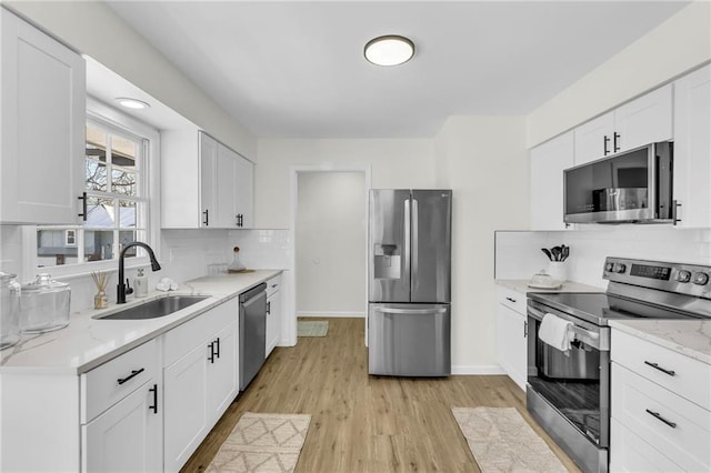 kitchen with white cabinetry, stainless steel appliances, light stone countertops, and sink