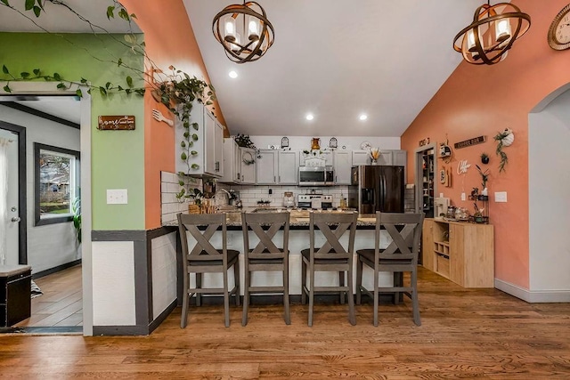 kitchen with stainless steel appliances, decorative light fixtures, kitchen peninsula, and light hardwood / wood-style floors